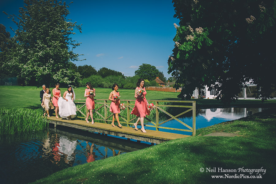 Bride arrives at the outdoor wedding ceremony by crossing the bridge at Ardington House