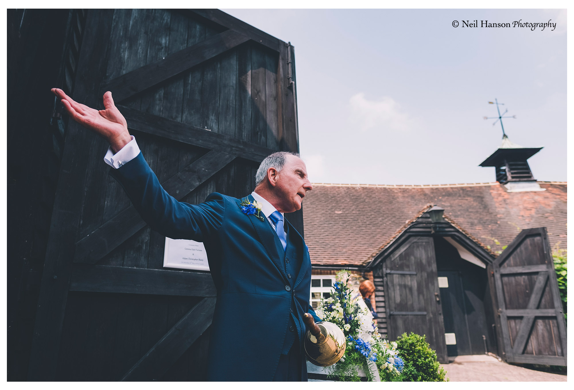 Father of the groom welcomes the wedding guests into the ceremony barn at Old Luxters Barn